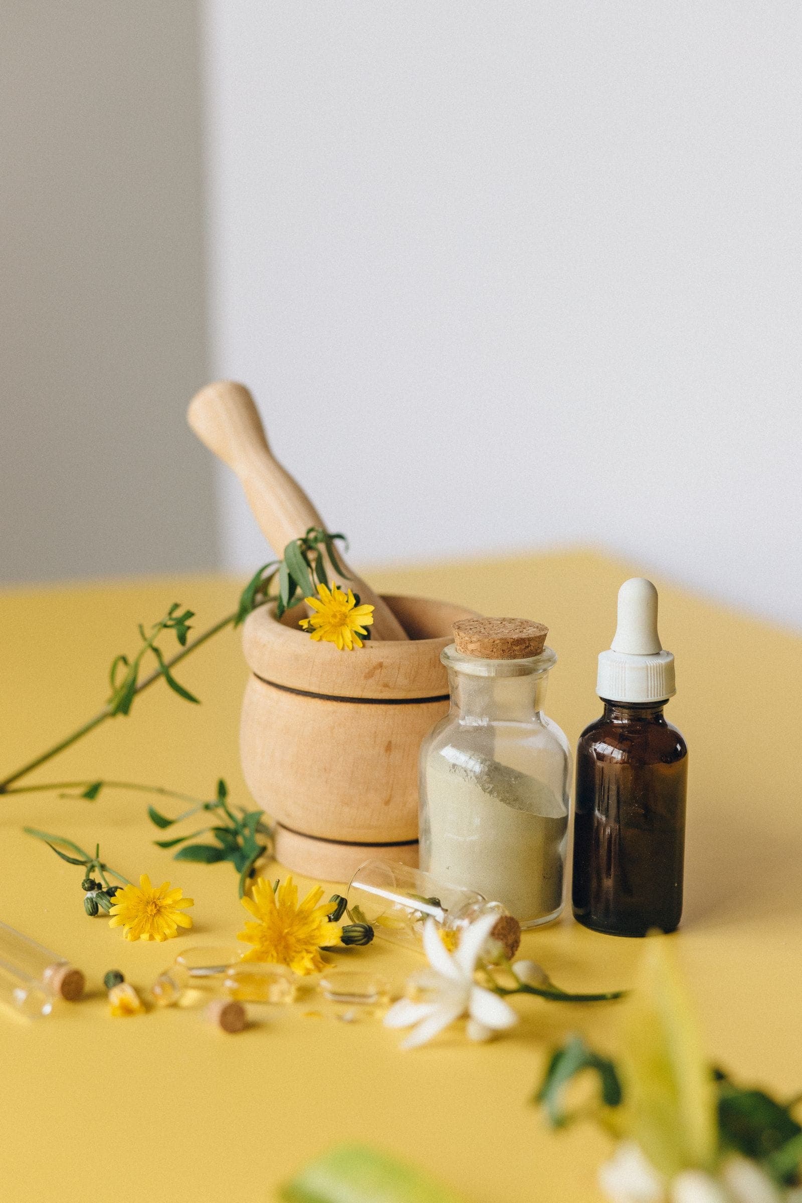 A wooden mortar and pestle with dandelion, a dropper bottle and a jar of remedy